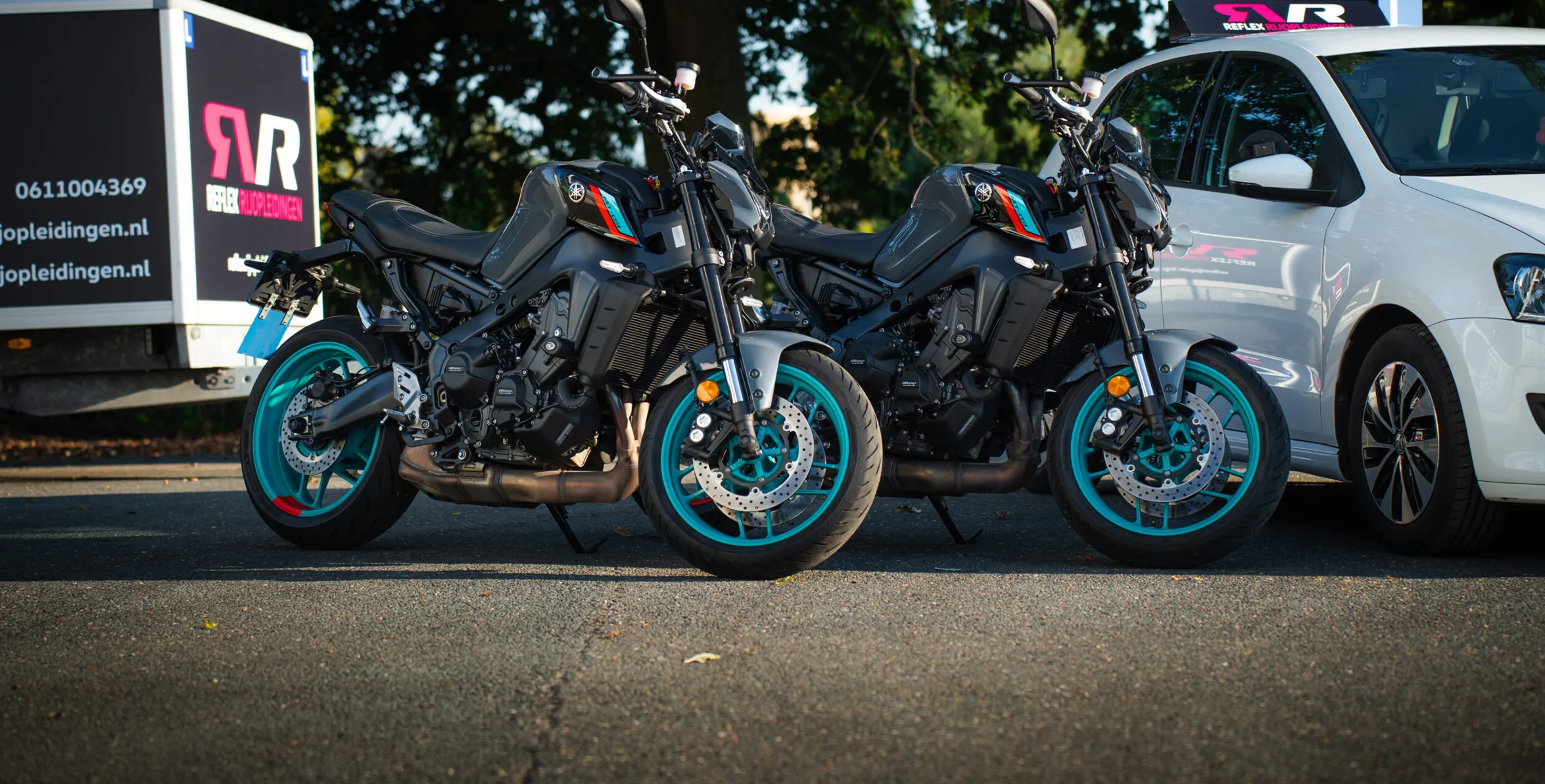 Twee moderne Yamaha lesmotoren van Reflex Rijopleidingen geparkeerd naast een lesauto, klaar voor jouw motorrijles.